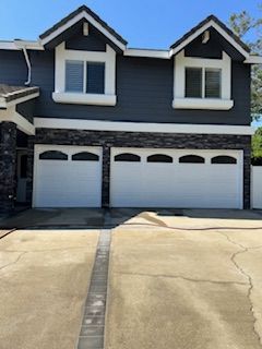 Two-story house with dark blue siding, white trim, and white garage doors. Stone accent above garage.