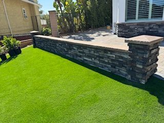 Stone retaining wall with artificial green grass in front.