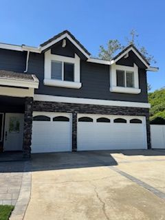 Two-story home with dark gray siding, white trim, two garage doors, and a paved driveway.