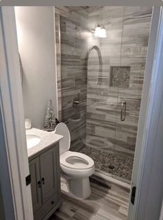 Bathroom with gray vanity, toilet, and glass shower with gray tile.