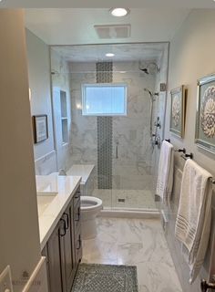 Bathroom with marble tile, glass shower, vanity, and a window. Towels and art adorn the walls.