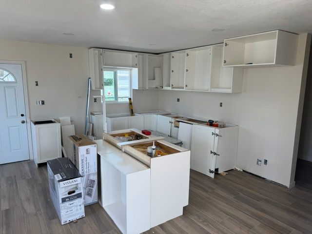 Kitchen under construction with white cabinets, island, and wooden floors.