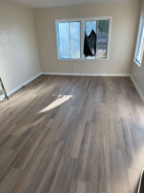 Empty room with wood-look flooring, light-colored walls, and windows with covering.