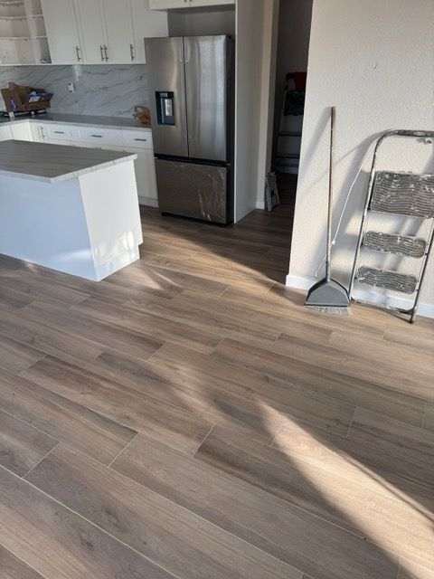 Kitchen with wood-look tile flooring, stainless steel refrigerator, white cabinets, and a step stool.