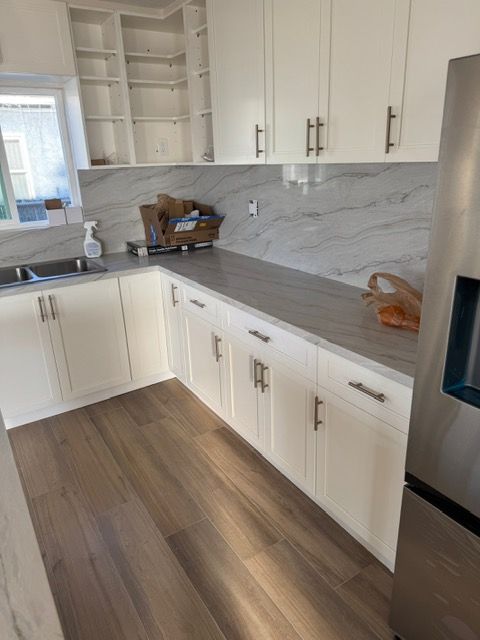 White kitchen with marble backsplash and wood flooring. Cabinets and refrigerator visible.