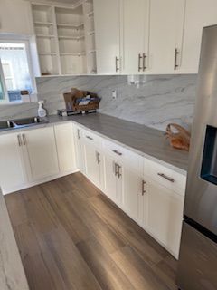 White kitchen with gray countertops, wood-look flooring, and stainless steel appliances.