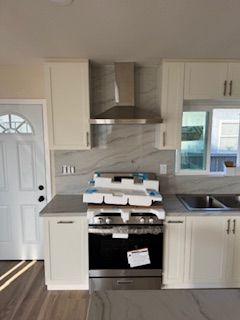 Kitchen with white cabinets, stainless steel range and hood, light countertops, and a window.