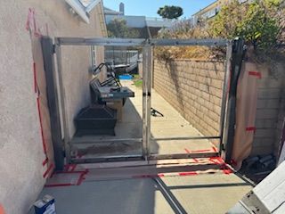 Metal gate installed in a narrow passageway between a stucco wall and a brick wall. Red tape marks the ground.