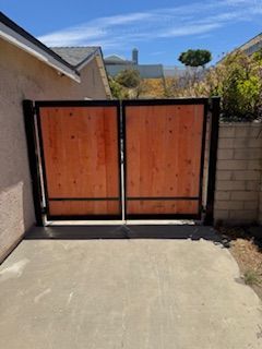 Double wooden gate with black frame, set in concrete, against a blue sky.