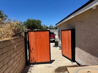 Open orange wooden gates in a narrow alley between a brick wall and a building with a red vehicle visible.