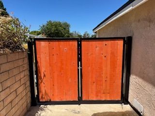 Orange wooden gate with black frame, between brick wall and beige stucco, under a blue sky.