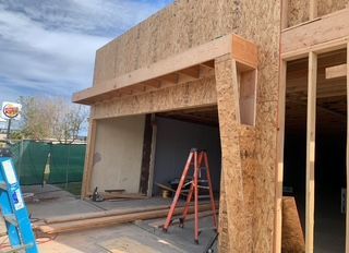 Construction site: plywood-covered building exterior with open doorway; orange ladder inside.