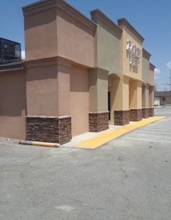 Exterior of a commercial building with tan and brown stucco walls, stone accents, and a yellow pedestrian ramp.