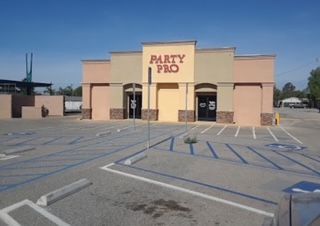 Party Pro store exterior with empty parking lot, tan and peach color scheme, clear blue sky.