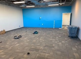 An empty room with blue and white walls, gray carpet, and debris.