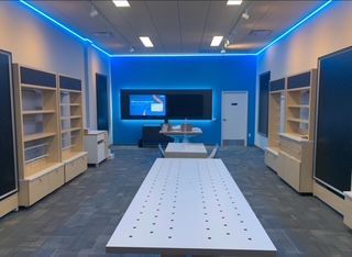 Interior of a bright blue and white retail store, featuring display tables and shelves with blue LED lighting.