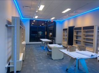 Empty store interior with blue neon lights along the ceiling, display shelves, and work tables.