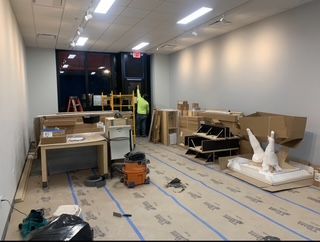 Interior of a room under construction with work materials and a person working; neutral colors.