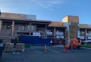 Building under construction with wooden frame, blue tarp, and construction equipment.