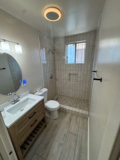 Bathroom with a wooden vanity, a shower with stone flooring, and a small window.