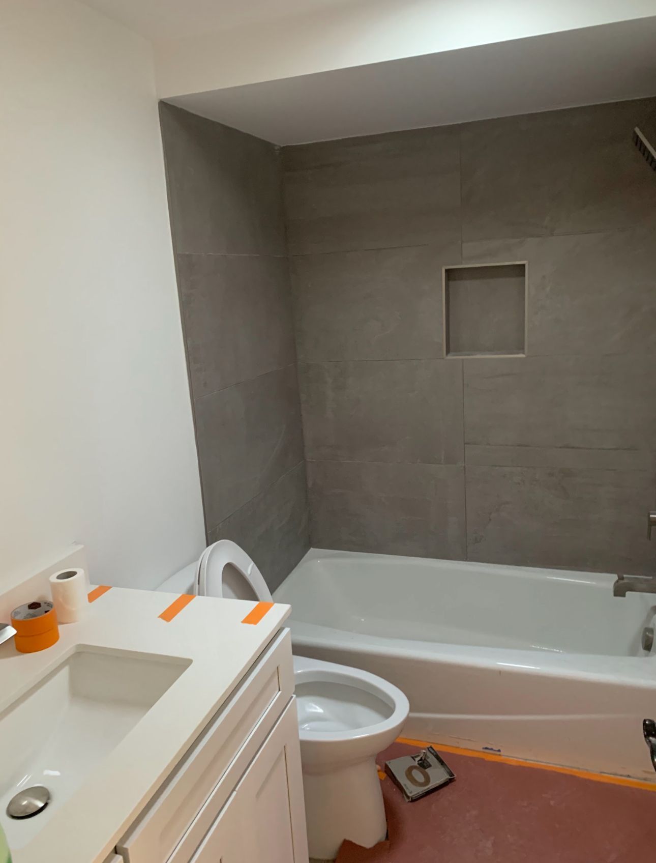 Bathroom with white sink and toilet, gray tiled shower with built-in niche, and white tub.