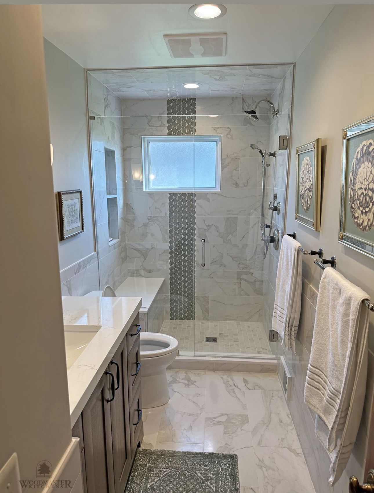 Modern bathroom with marble tile, glass shower, double vanity, and towel racks.