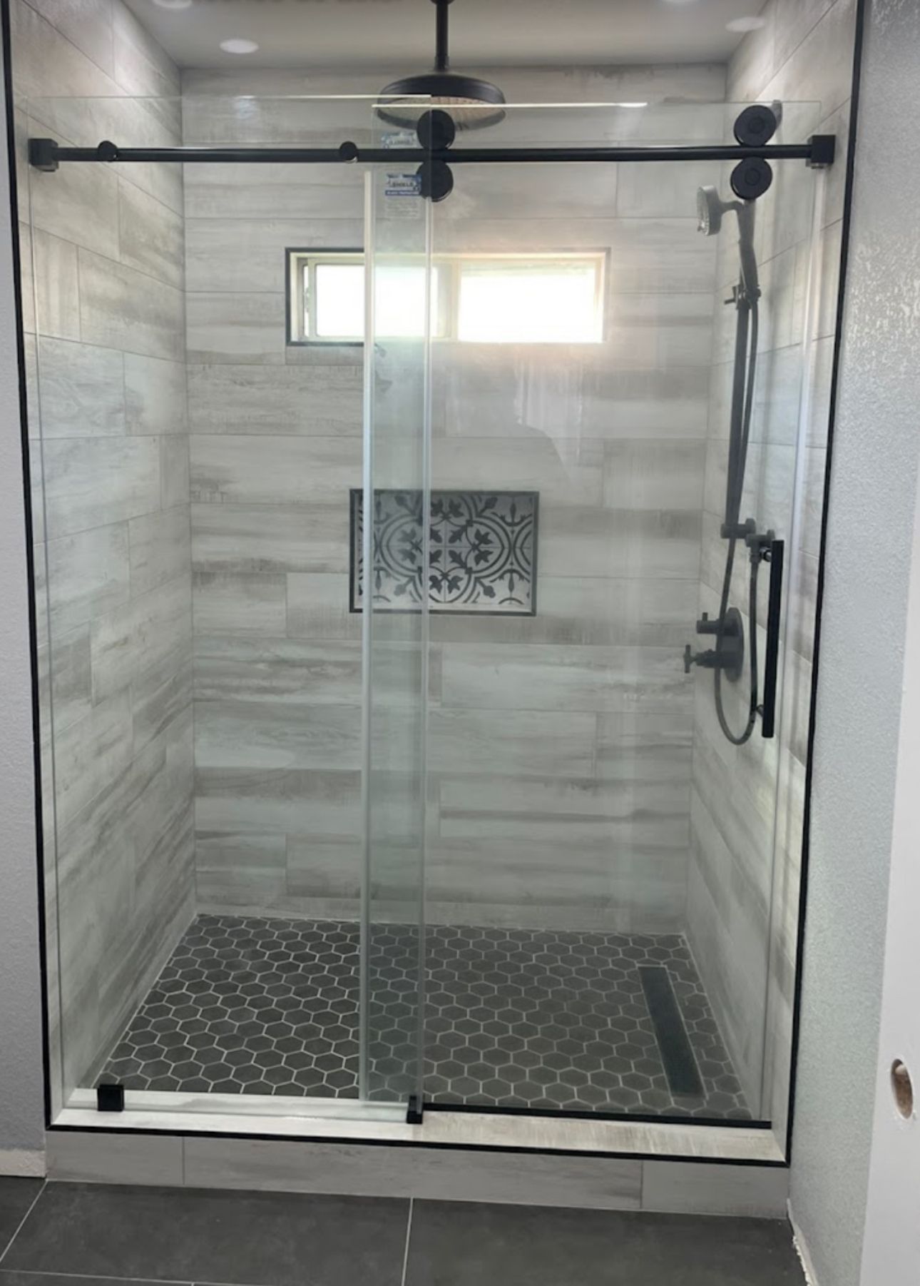 Modern shower with glass door, black fixtures, gray and black tile.