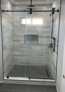 Modern shower with glass door and black fixtures; gray tiled walls and floor.