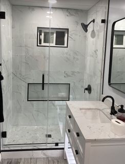 Modern bathroom with marble walls, glass shower door, black fixtures, and white vanity.