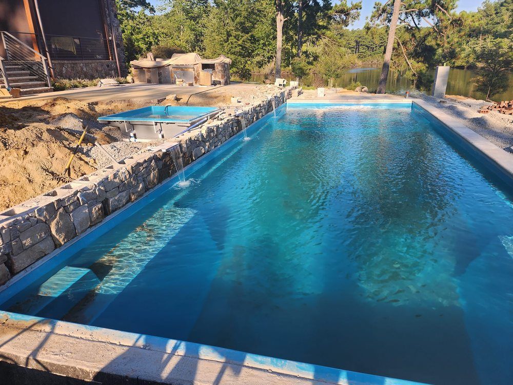A large swimming pool is surrounded by a stone wall and trees.