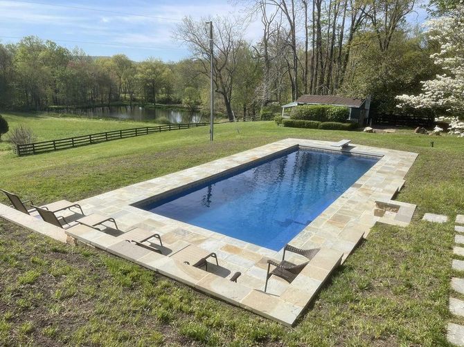 There is a large swimming pool in the middle of a lush green field.