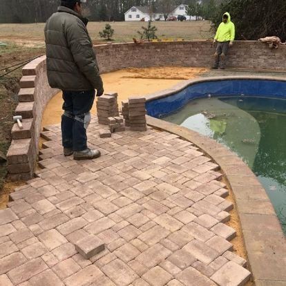 A man is standing on a brick walkway next to a swimming pool.