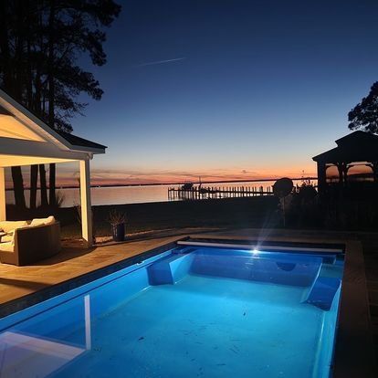 A swimming pool is lit up at night with a gazebo in the background