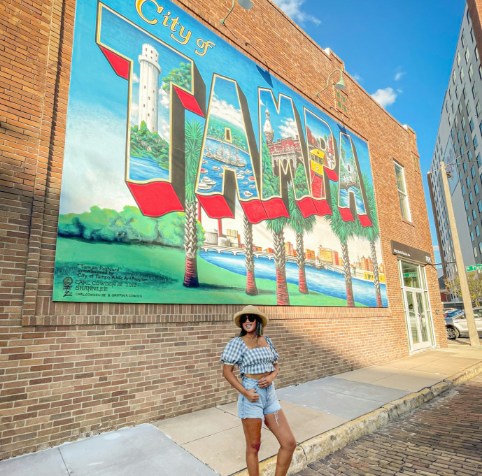 A woman is standing in front of a large mural of the city of tampa
