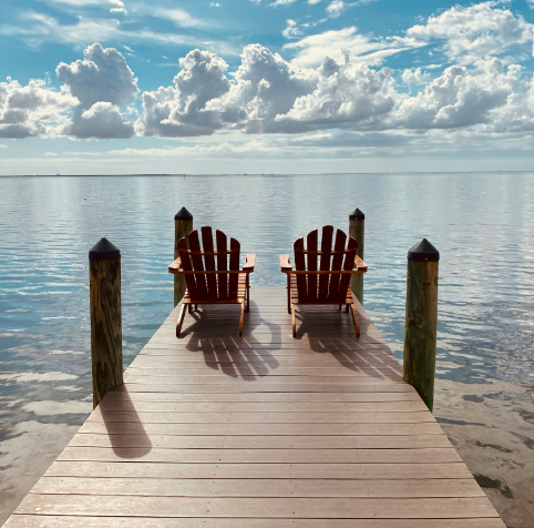 Two adirondack chairs on a dock overlooking the ocean