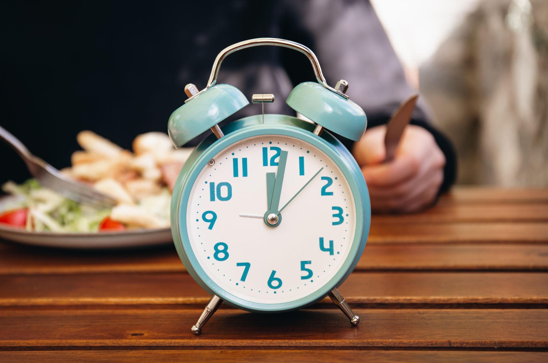 um relógio despertador com um prato de almoço ao fundo