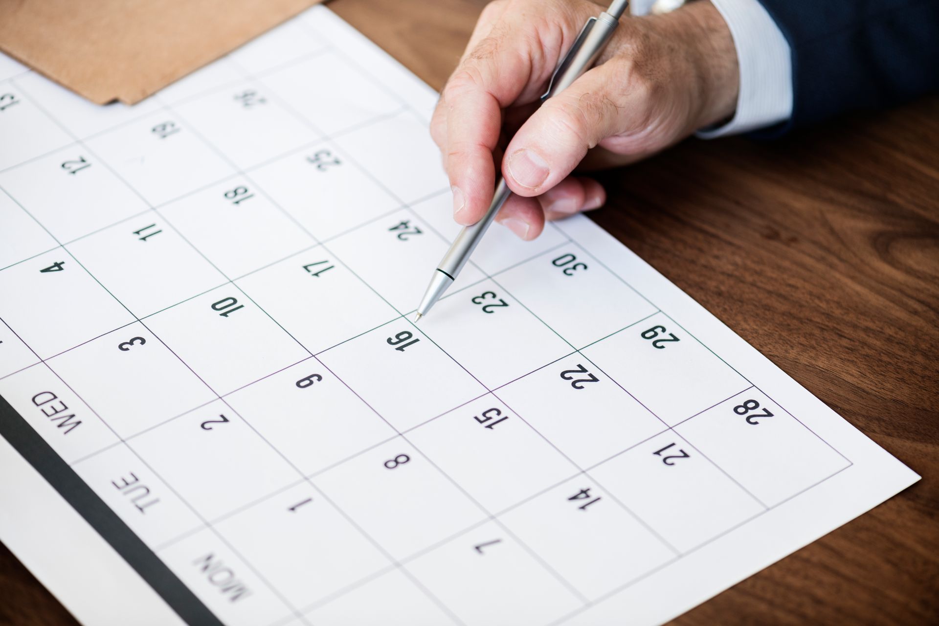 Uma mão segura uma caneta enquanto aponta para uma data em um calendário