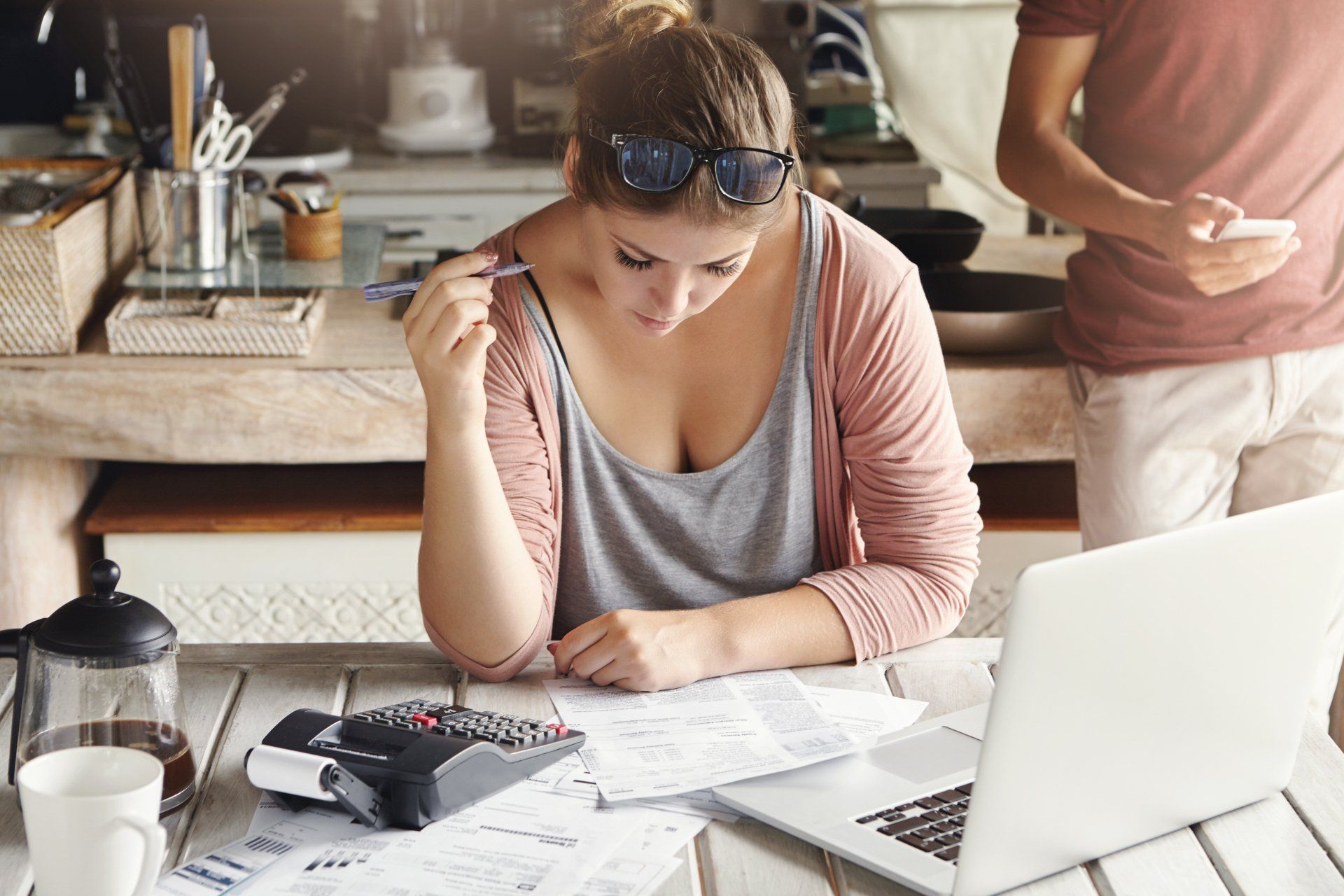 Mulher sentada em uma cadeira e mesa de frente para um notebook e uma calculadora olhando para um papel