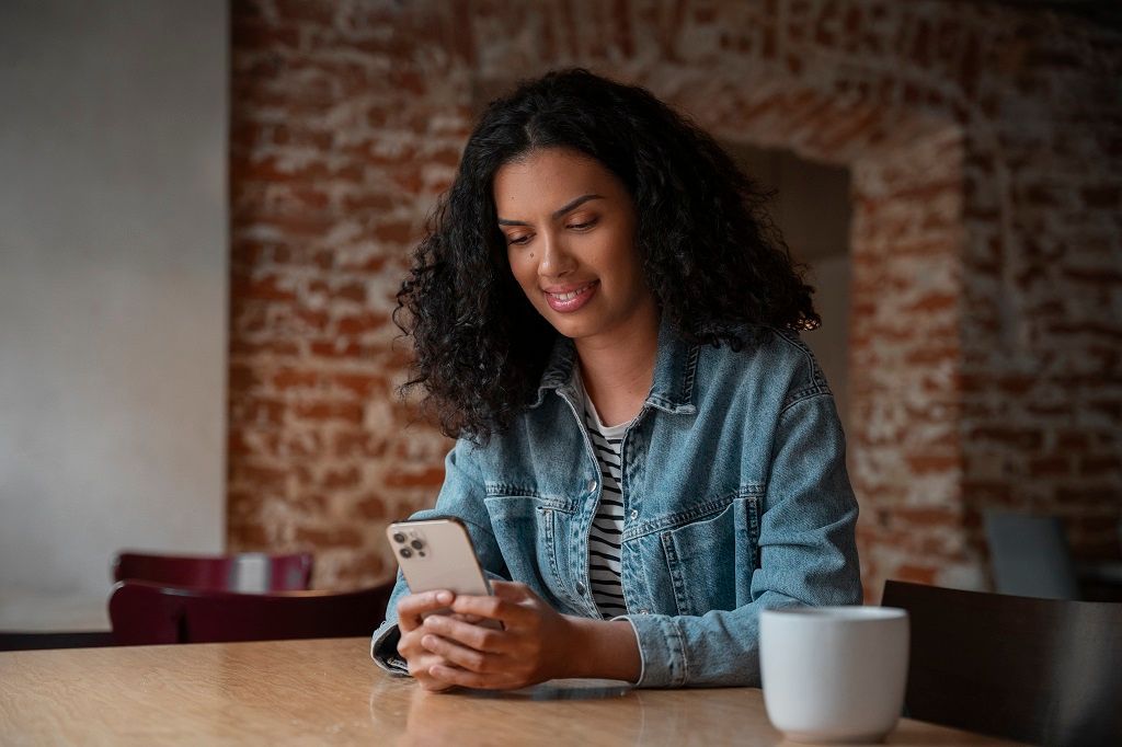 Uma mulher de cabelo cacheado está sentada mexendo no celular