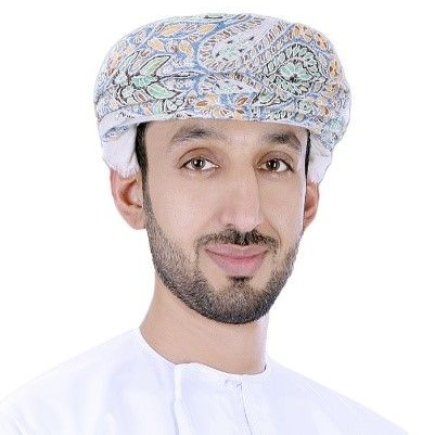 Man in a white Omani dishdasha and patterned turban smiling at the camera.