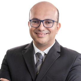 Man with glasses in a suit smiling, arms crossed. Studio shot against a white background.