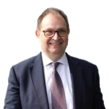 Man wearing glasses, suit, and tie smiling, facing the camera.