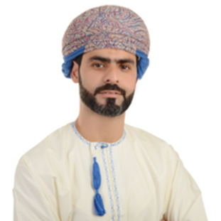 Man in traditional Omani dress, wearing a patterned turban and smiling slightly.