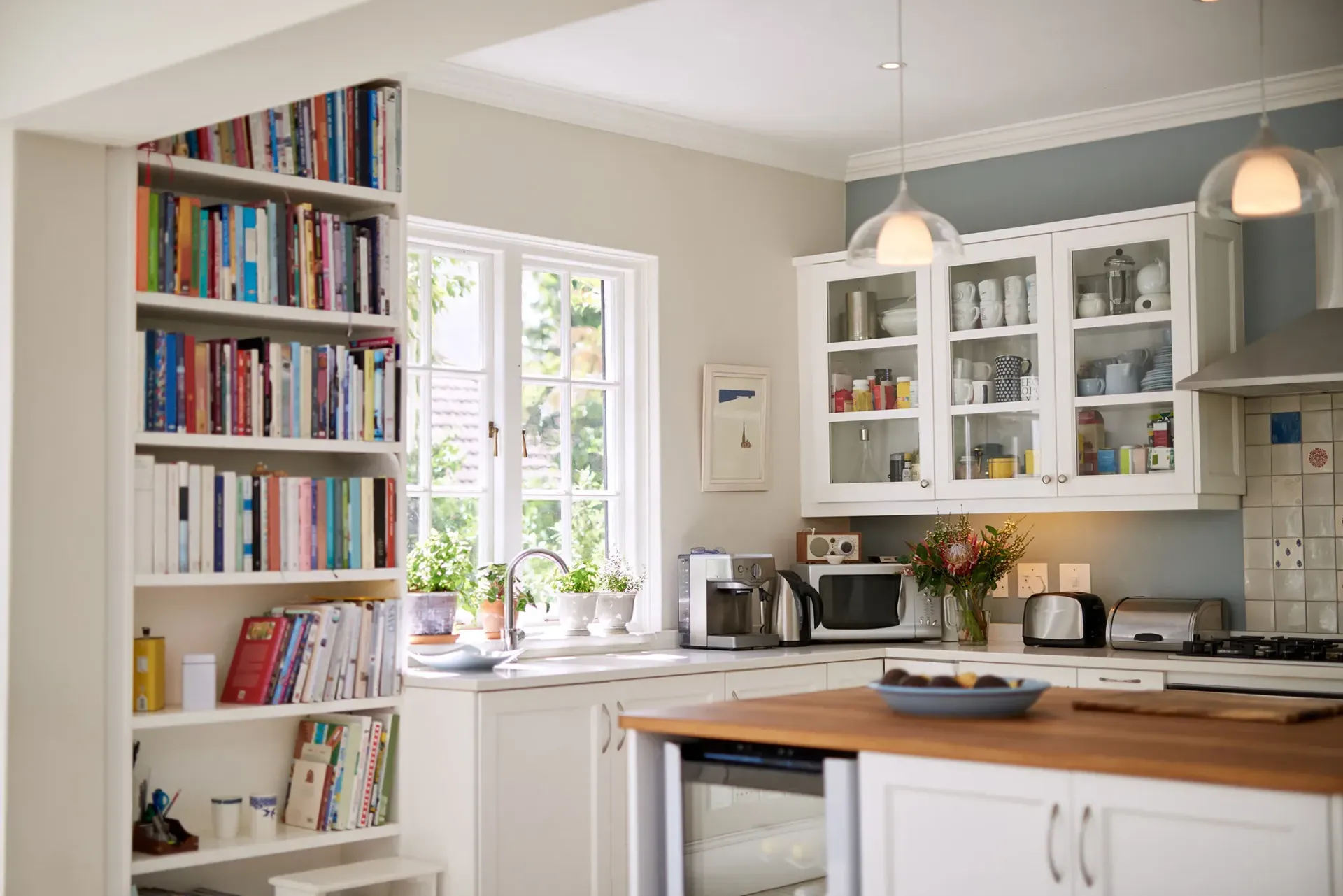 Kitchen interior with white cabinets, built-in bookshelf, window, and small island.