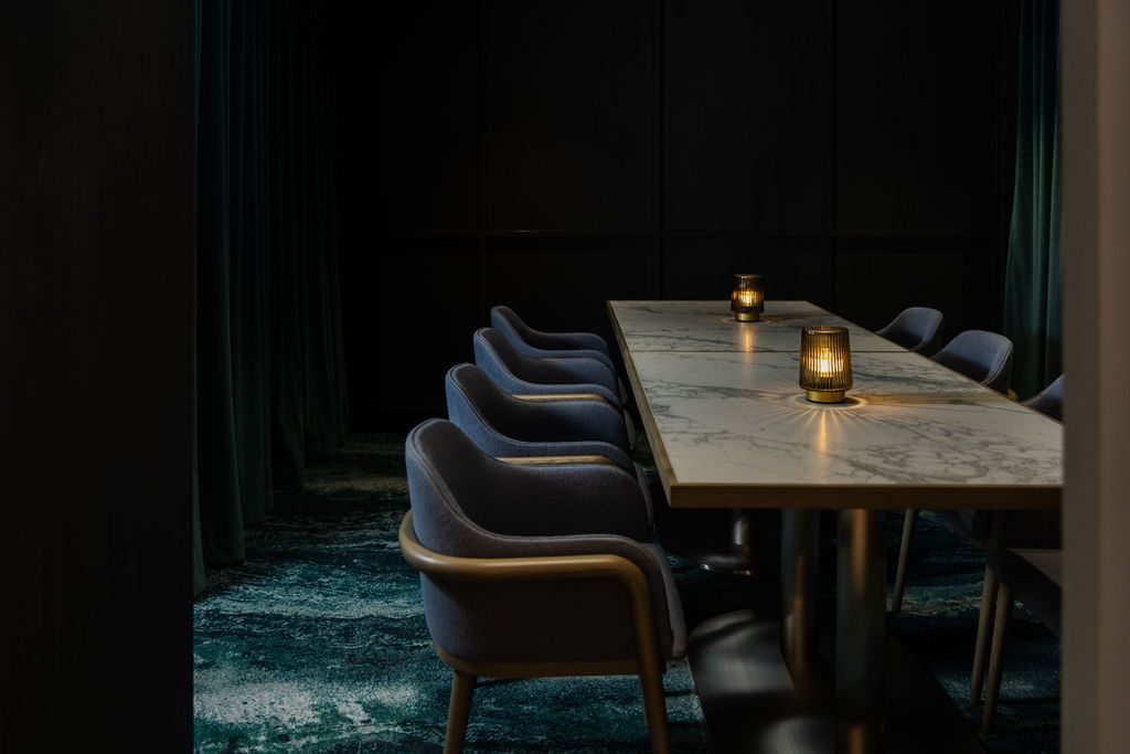 Dark dining room with a long table, eight chairs, and two lit candles.
