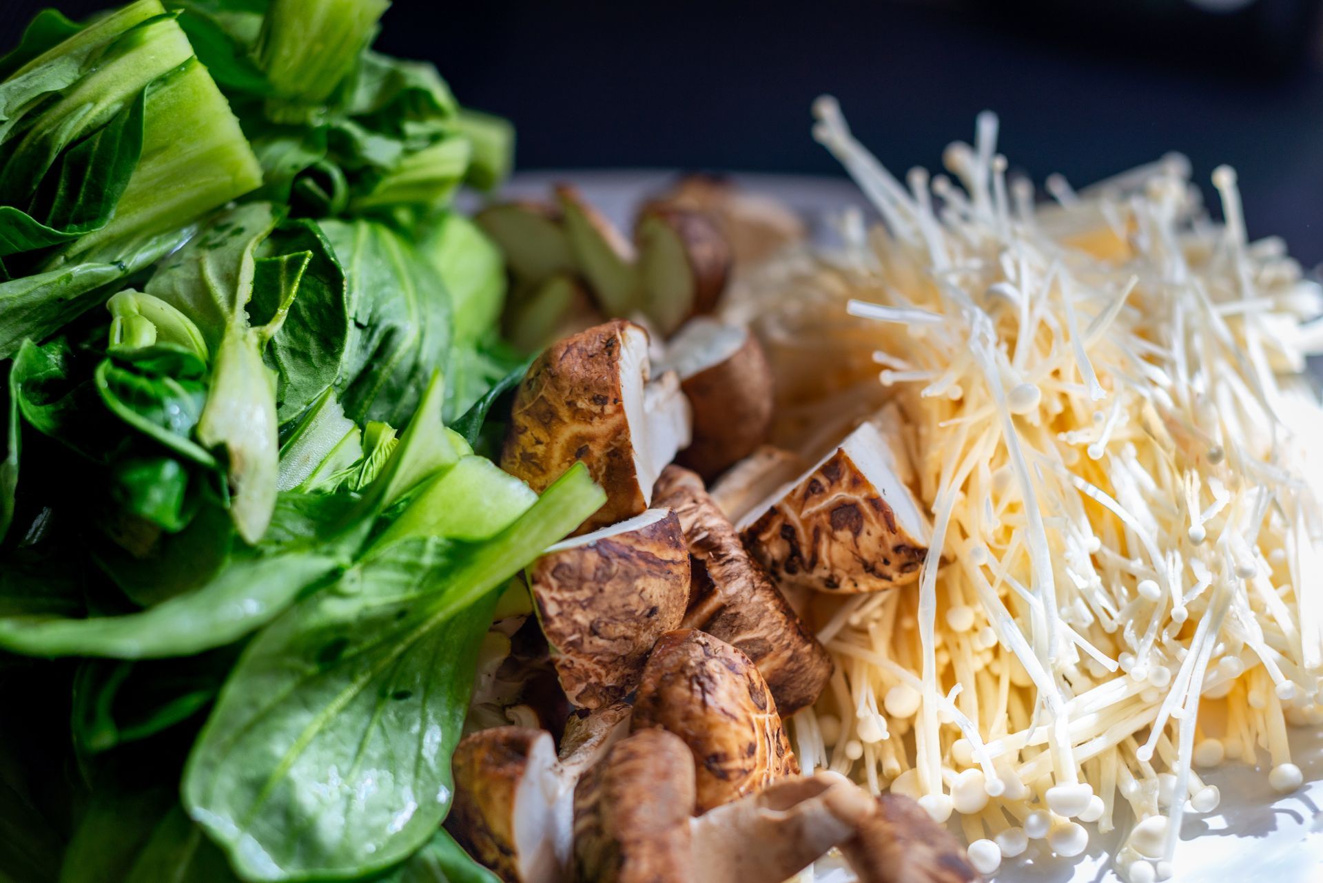 Chopped bok choy, shiitake mushrooms, and enoki mushrooms prepared for cooking.