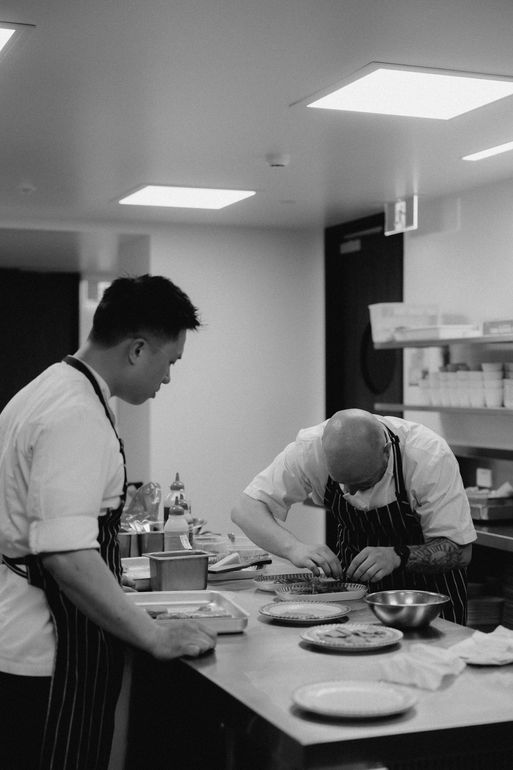 Chef plates a dish in a commercial kitchen, wearing apron and chef's whites.