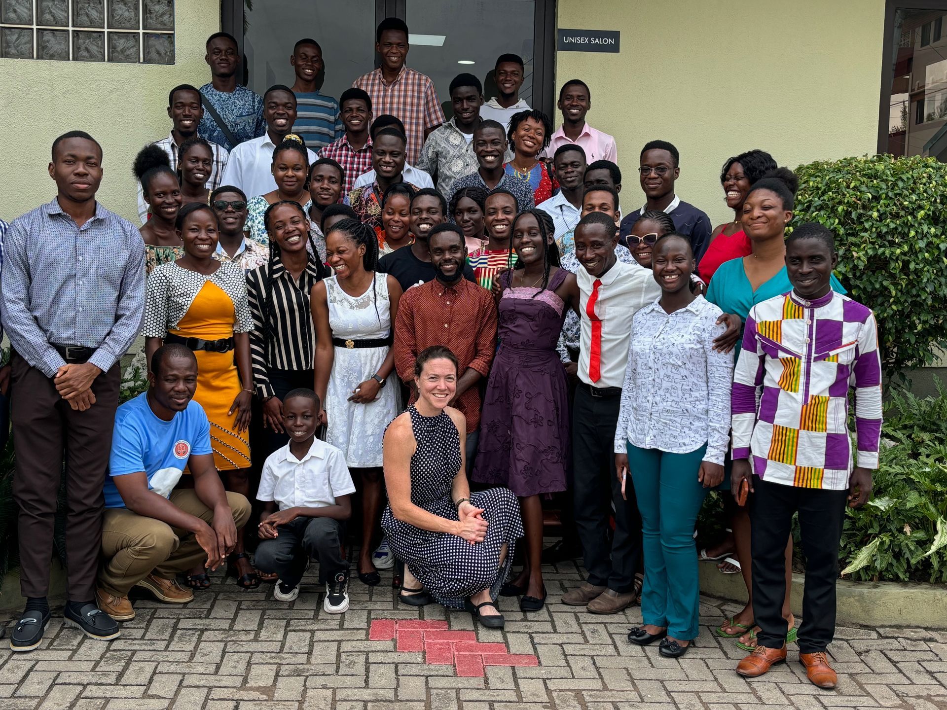 Group of people outside a building. Many smiling, diverse individuals. Some are standing, others kneeling.