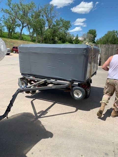 A man is pushing a trailer with a large gray box on it