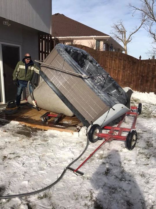 A man is pushing a hot tub on a cart in the snow